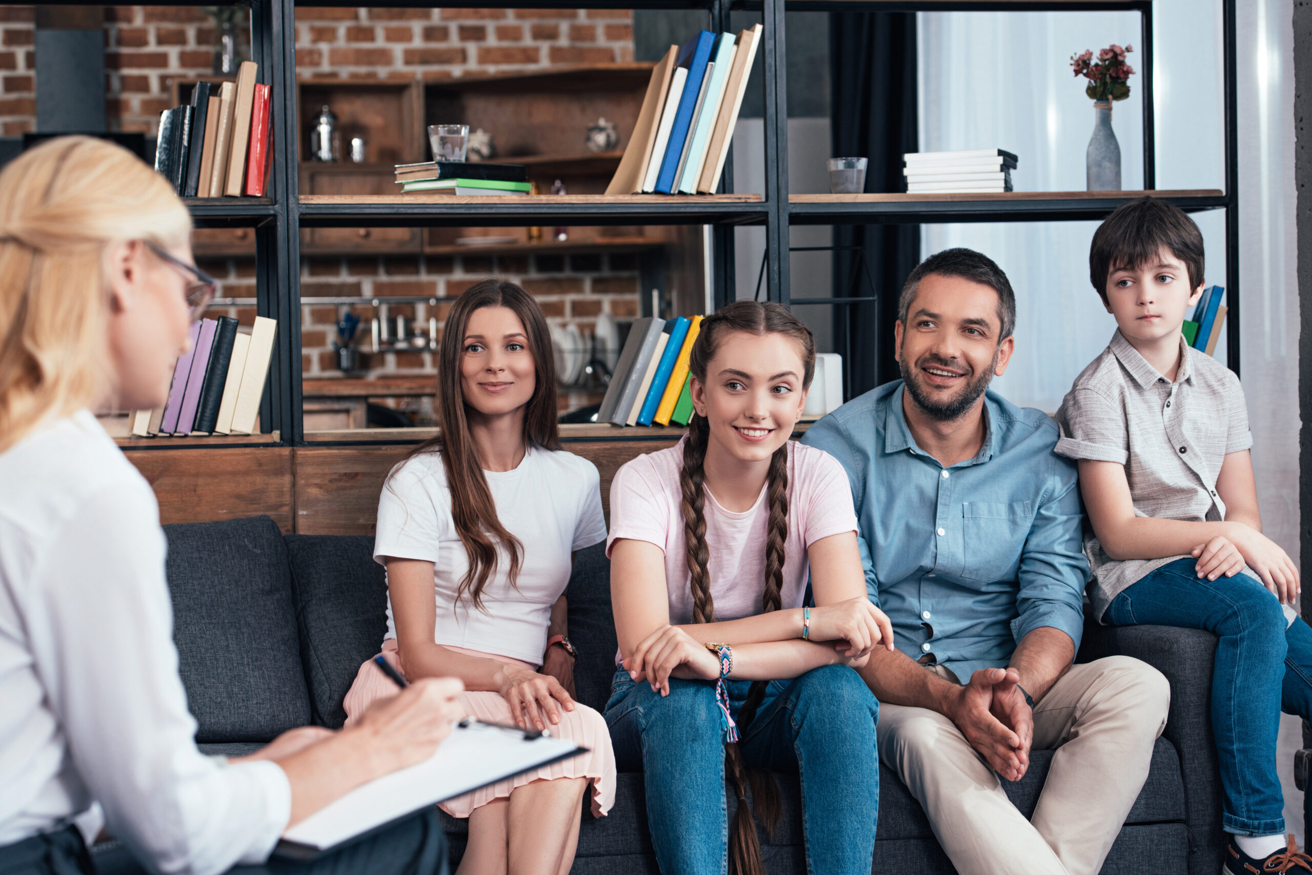 A family with two young girls, a father and a son talking to a therapist in family therapy.