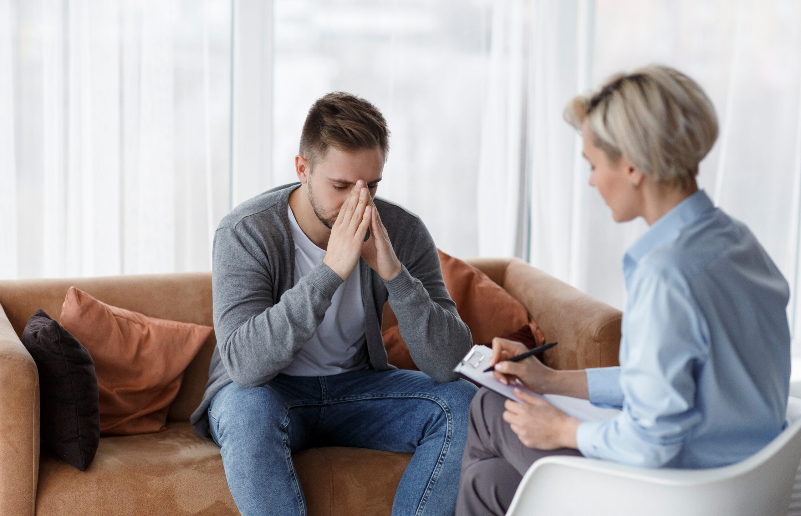 Worried man holding his face talking to a female therapist.