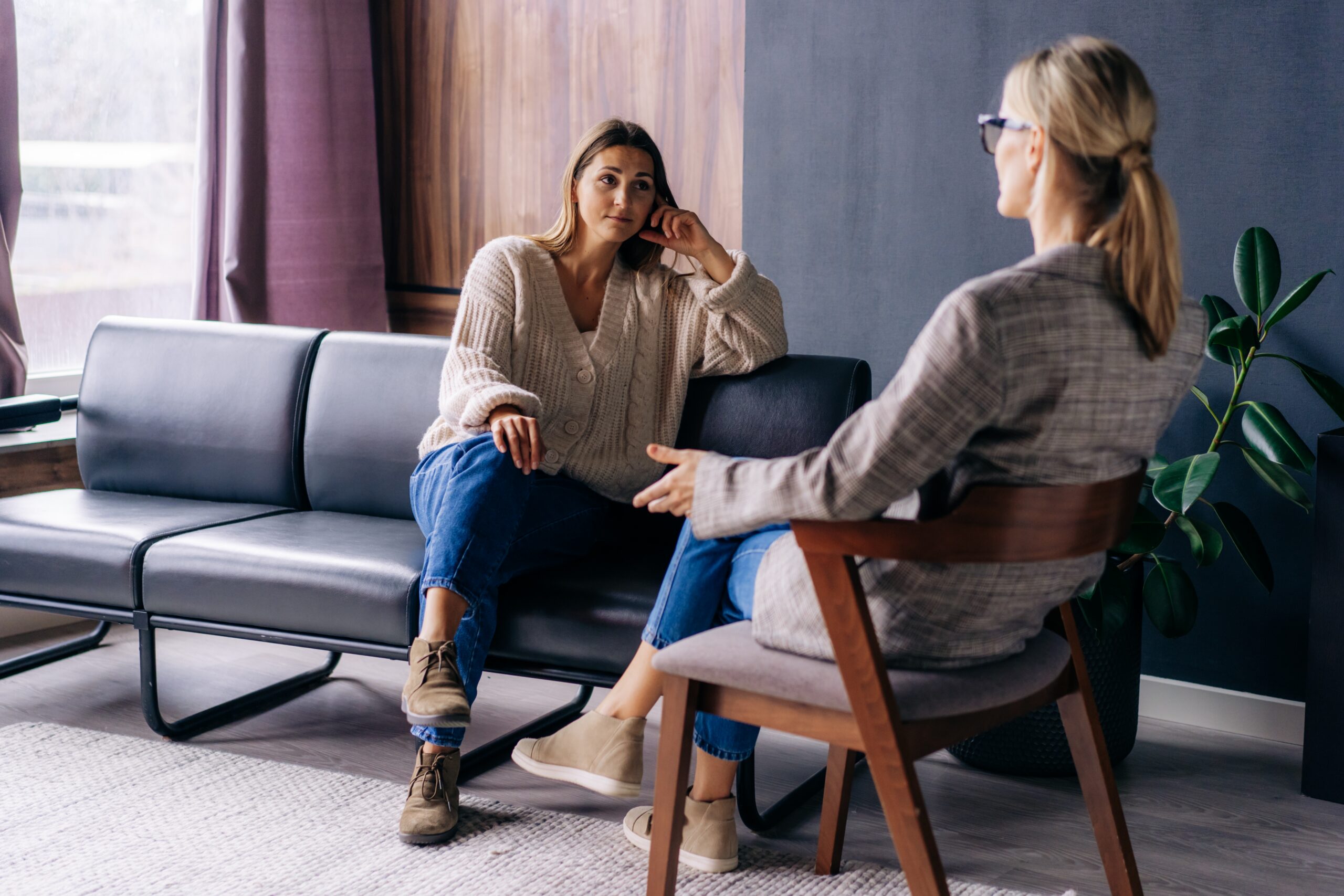 A young woman sitting on a couch talking to a female therapist.