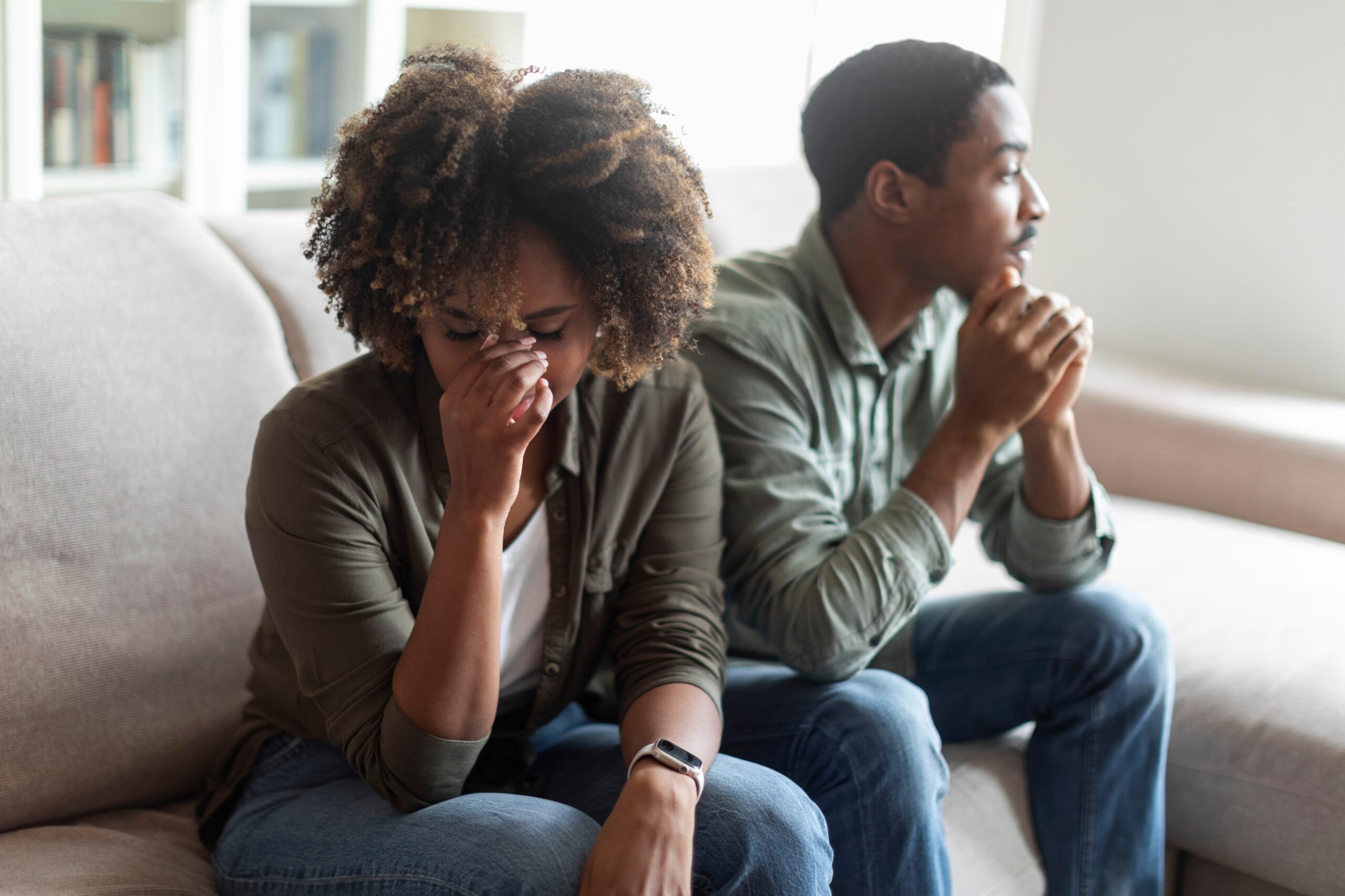 African American couple sitting on a couch and the woman is upset, holding her face.