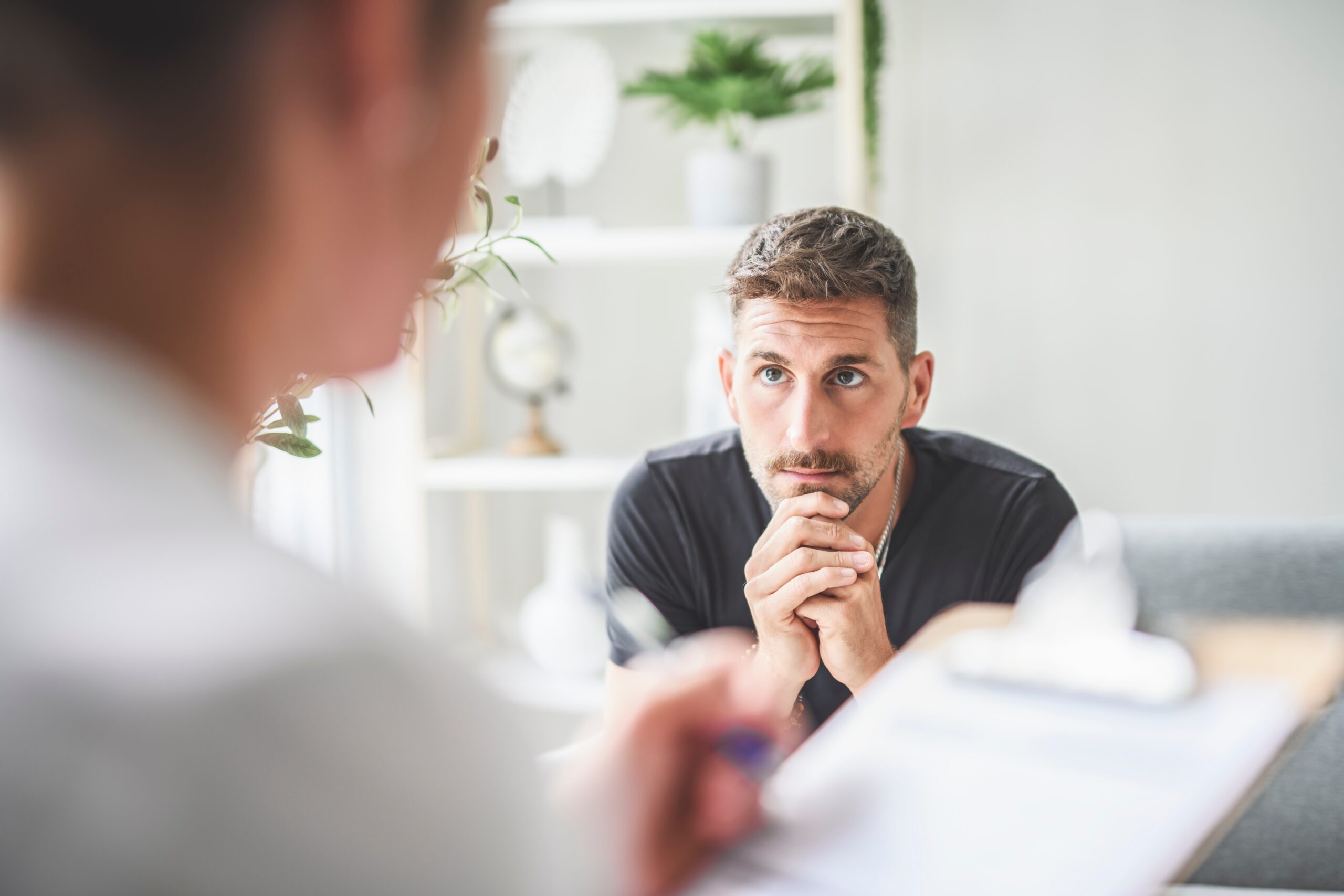 Man looking worried talking to a female therapist holding a clipboard.